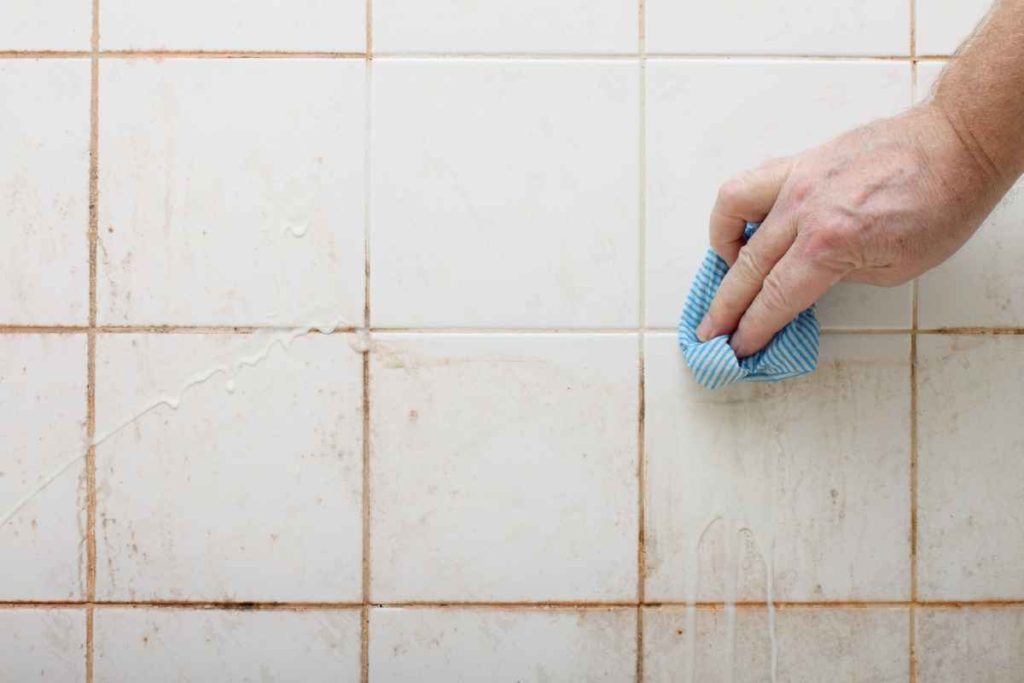 Hand scrubbing mouldy bathroom tiles to remove buildup in a Sydney home bathroom
