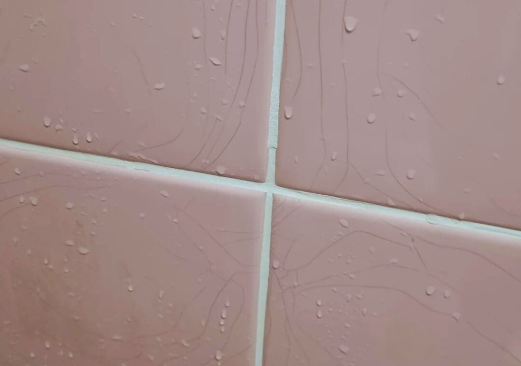 Cracked pink wall tiles with visible water droplets