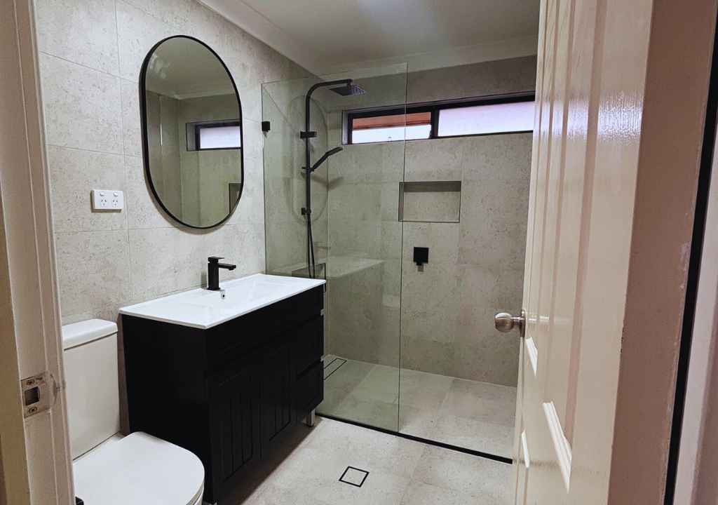 Renovated Sydney bathroom featuring walk-in shower, matte black fixtures, and wall-hung vanity—highlighting proper drainage and waterproofing by Empire Tiles.