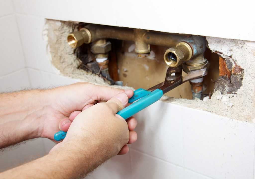 Repairing leaking bathroom pipes behind a tiled Sydney wall, showing hidden plumbing damage